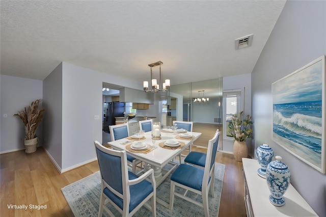 dining area with a textured ceiling, light hardwood / wood-style flooring, and a notable chandelier