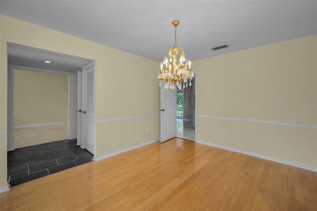 empty room with wood-type flooring and an inviting chandelier