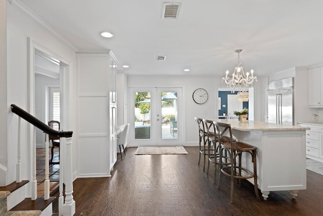 kitchen with built in refrigerator, white cabinetry, a kitchen breakfast bar, decorative light fixtures, and french doors