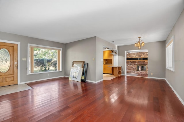 unfurnished living room with a stone fireplace, a chandelier, and hardwood / wood-style floors