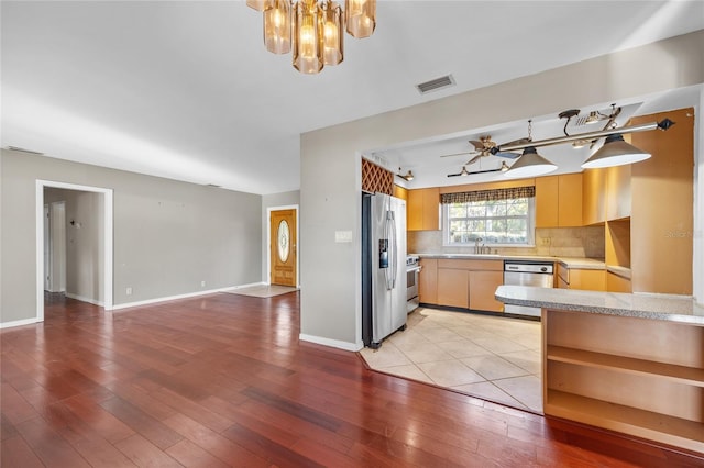 kitchen featuring stainless steel appliances, ceiling fan with notable chandelier, decorative backsplash, and light hardwood / wood-style flooring