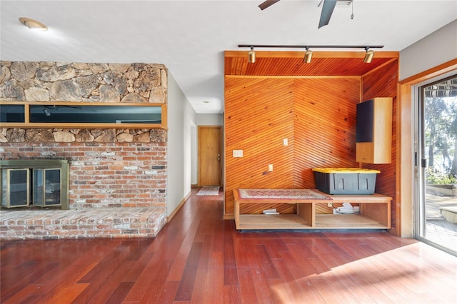 interior space with a brick fireplace, dark wood-type flooring, ceiling fan, and wood walls