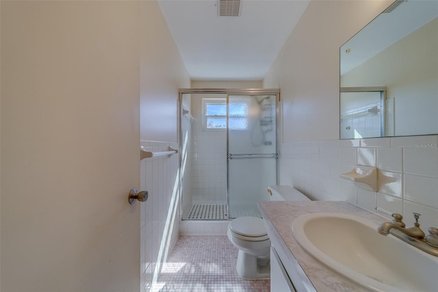 bathroom with toilet, tile walls, vanity, and a shower with shower door