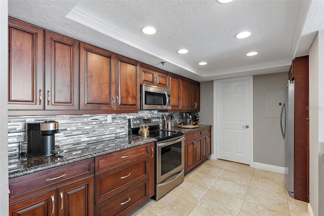 kitchen with appliances with stainless steel finishes, a raised ceiling, decorative backsplash, and dark stone counters