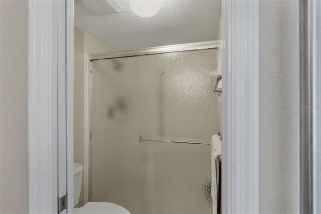 bathroom featuring an enclosed shower, a textured ceiling, and toilet