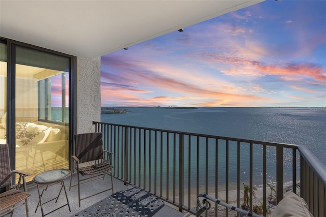 balcony at dusk featuring a water view