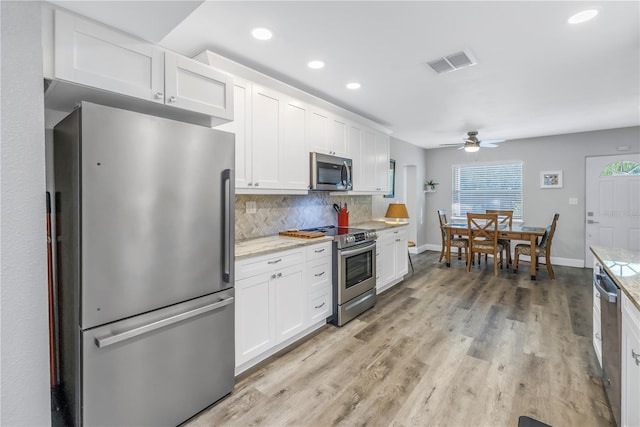 kitchen with stainless steel appliances, light hardwood / wood-style flooring, decorative backsplash, and white cabinets