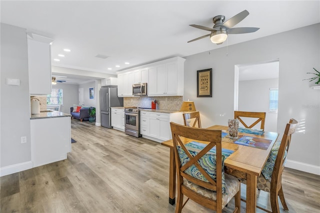 kitchen with white cabinets, backsplash, ceiling fan, stainless steel appliances, and light wood-type flooring