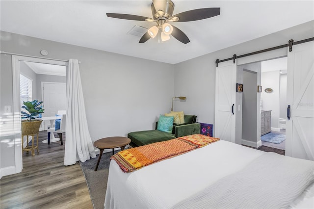 bedroom featuring dark wood-type flooring, ceiling fan, a barn door, and ensuite bath