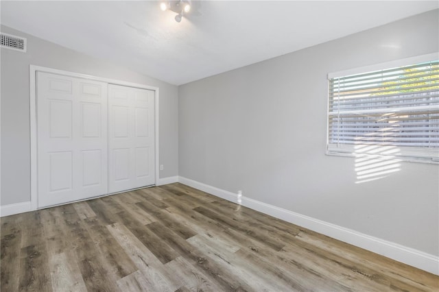 unfurnished bedroom with hardwood / wood-style flooring, lofted ceiling, and a closet