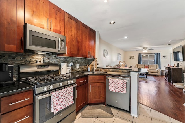 kitchen with sink, stainless steel appliances, light tile patterned flooring, decorative backsplash, and dark stone counters