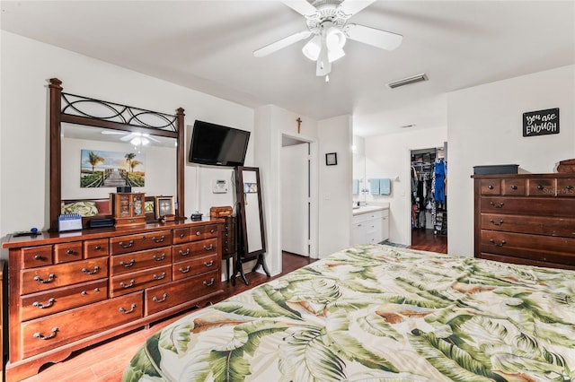 bedroom with ensuite bath, dark wood-type flooring, ceiling fan, a walk in closet, and a closet