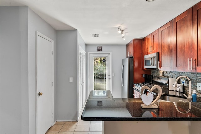 kitchen with light tile patterned flooring, sink, dark stone countertops, kitchen peninsula, and stainless steel appliances