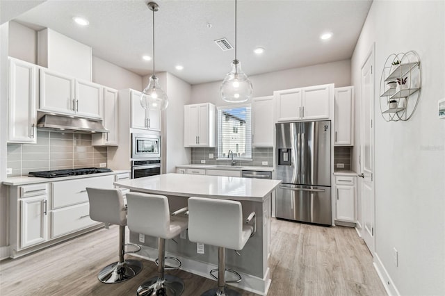 kitchen with a kitchen island, pendant lighting, white cabinetry, a breakfast bar area, and stainless steel appliances