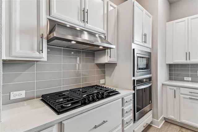 kitchen featuring ventilation hood, white cabinetry, backsplash, stainless steel appliances, and light stone countertops