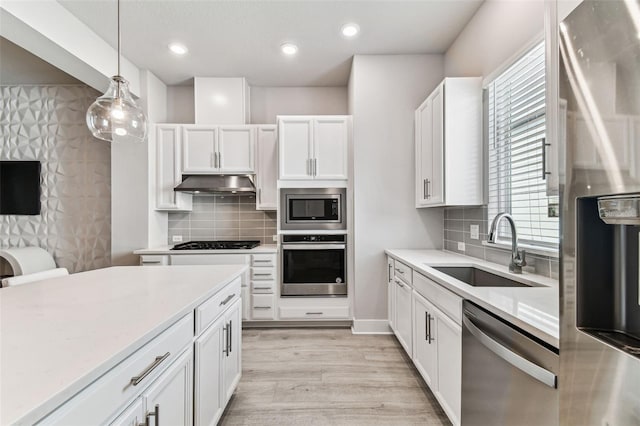 kitchen with sink, white cabinets, hanging light fixtures, stainless steel appliances, and light wood-type flooring