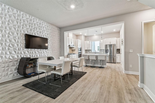 dining room featuring sink, a textured ceiling, and light wood-type flooring