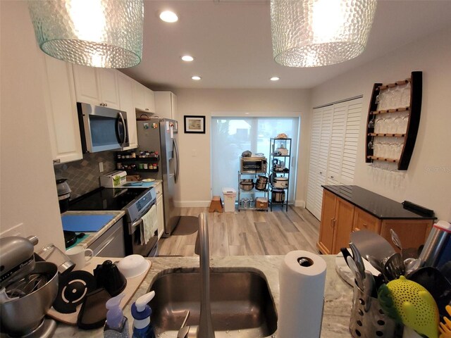 kitchen with sink, appliances with stainless steel finishes, white cabinetry, tasteful backsplash, and light wood-type flooring