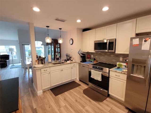 kitchen featuring sink, appliances with stainless steel finishes, kitchen peninsula, pendant lighting, and white cabinets