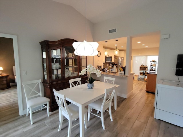 dining space featuring high vaulted ceiling and light hardwood / wood-style flooring