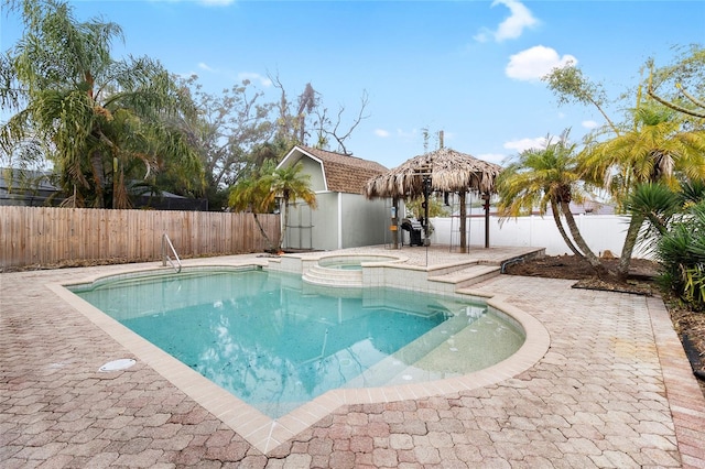 view of swimming pool with an outbuilding, a pool with connected hot tub, a storage shed, a patio area, and a fenced backyard