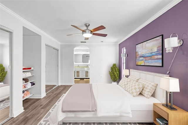 bedroom with ornamental molding, arched walkways, baseboards, and wood finished floors