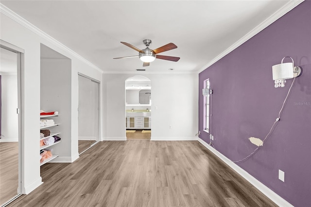 empty room featuring arched walkways, ceiling fan, ornamental molding, and wood finished floors