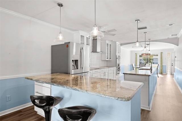 kitchen featuring stainless steel appliances, wood finished floors, a sink, wall chimney exhaust hood, and a large island with sink