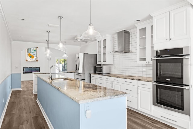 kitchen with tasteful backsplash, appliances with stainless steel finishes, a kitchen island with sink, a sink, and wall chimney exhaust hood