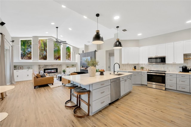 kitchen with sink, gray cabinetry, hanging light fixtures, a multi sided fireplace, and stainless steel appliances