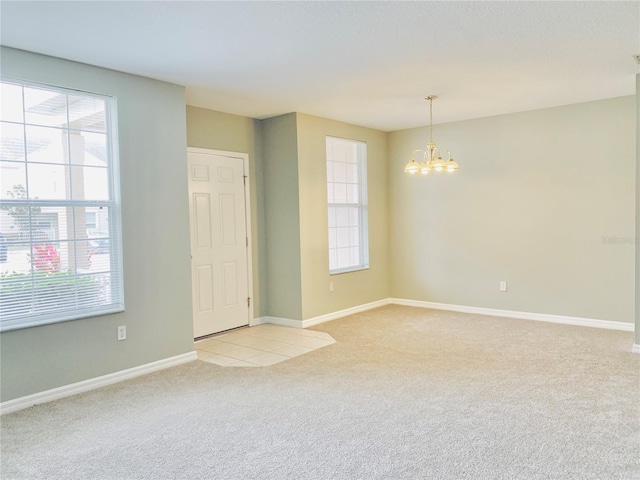 spare room featuring an inviting chandelier and light colored carpet