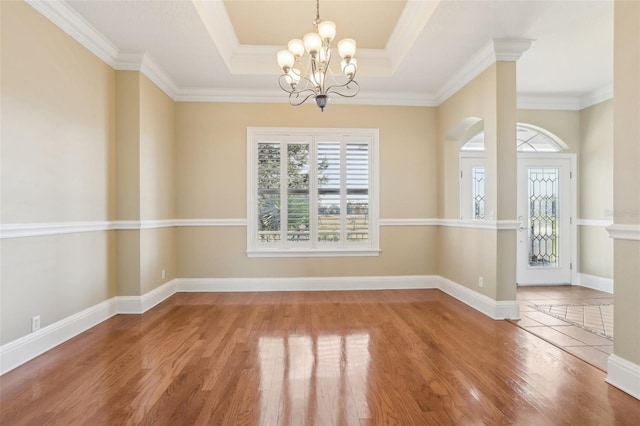 unfurnished dining area with wood-type flooring, ornamental molding, a chandelier, and a tray ceiling