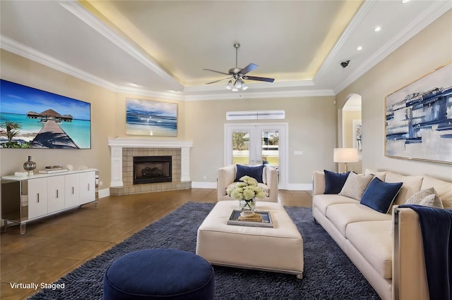 living room with ceiling fan, dark tile patterned floors, a fireplace, ornamental molding, and a raised ceiling