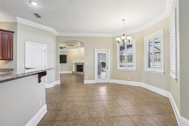 unfurnished dining area with a fireplace, ornamental molding, tile patterned floors, a textured ceiling, and an inviting chandelier