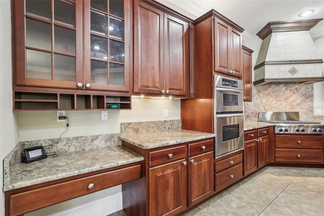 kitchen with premium range hood, backsplash, stainless steel appliances, light stone counters, and light tile patterned flooring