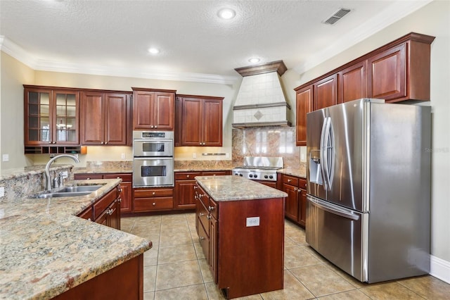 kitchen featuring premium range hood, appliances with stainless steel finishes, sink, a center island, and light stone counters