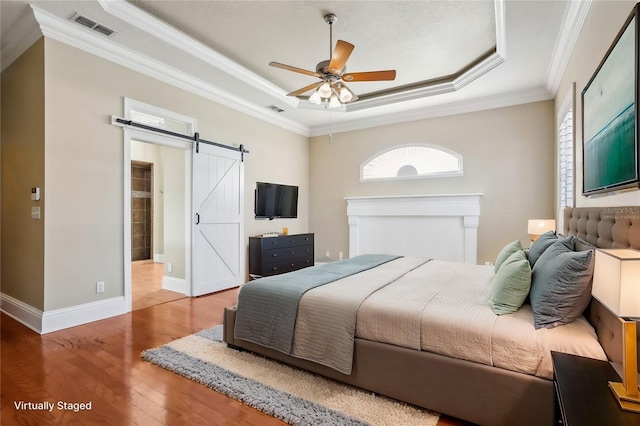 bedroom featuring crown molding, ceiling fan, a tray ceiling, wood-type flooring, and a barn door