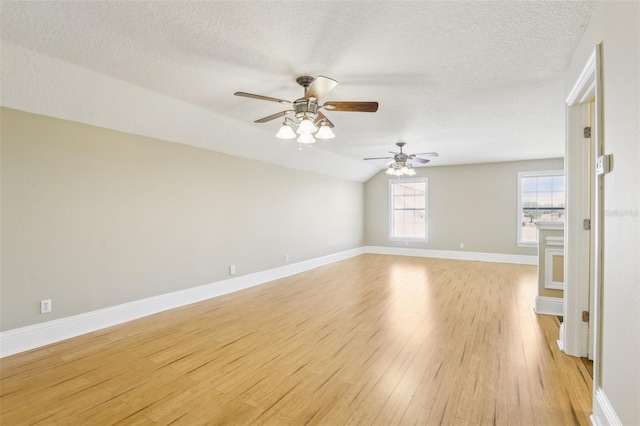 spare room featuring ceiling fan, vaulted ceiling, light hardwood / wood-style floors, and a textured ceiling