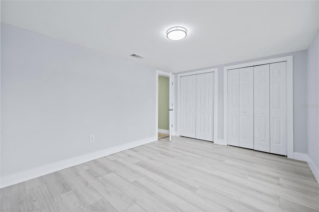 unfurnished bedroom featuring multiple closets and light hardwood / wood-style flooring