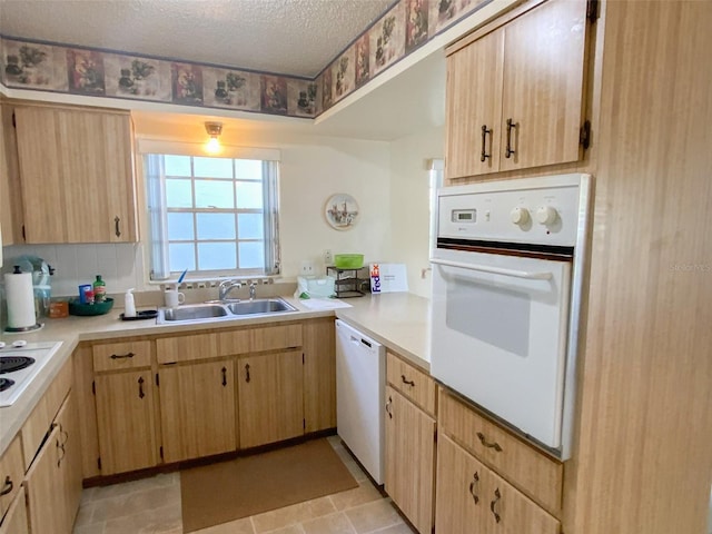 kitchen with white appliances, light brown cabinetry, sink, and a textured ceiling