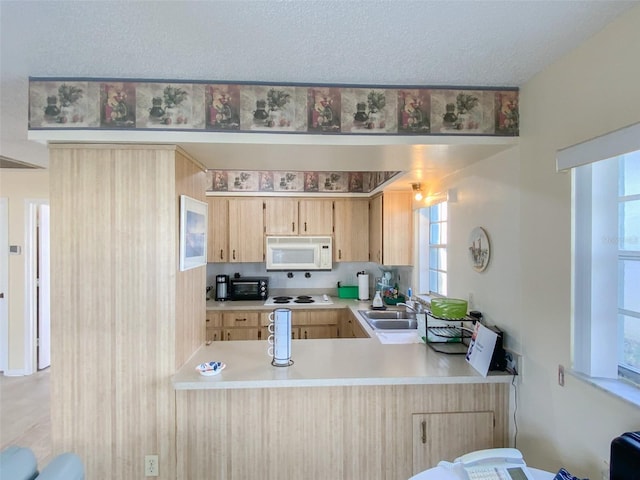 kitchen with light brown cabinetry, sink, a textured ceiling, kitchen peninsula, and white appliances