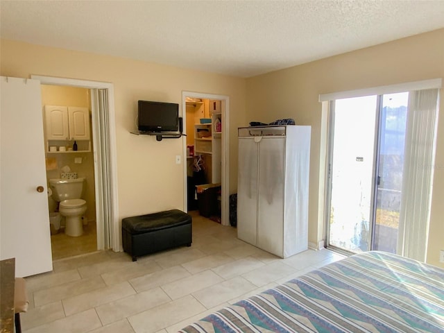 bedroom with connected bathroom, a walk in closet, light tile patterned floors, a textured ceiling, and a closet