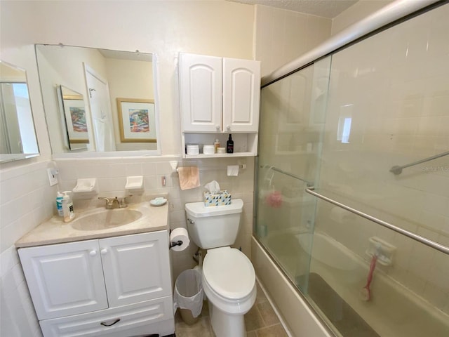 full bathroom featuring toilet, vanity, shower / bath combination with glass door, and tile walls