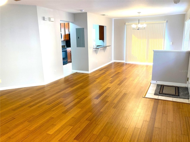 unfurnished living room featuring a chandelier, electric panel, and light wood-type flooring