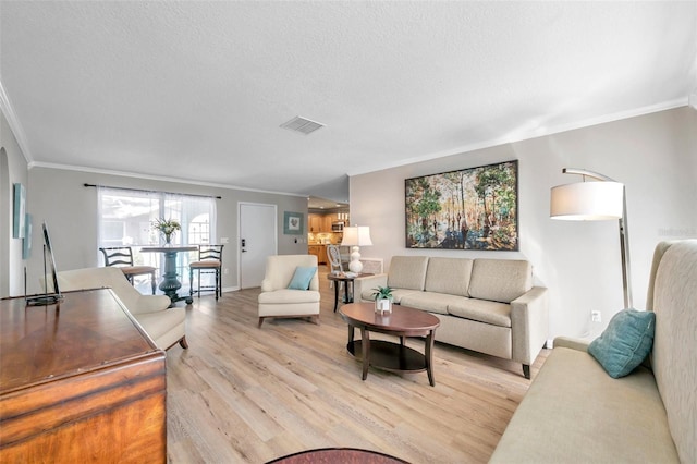 living room featuring light wood-type flooring, ornamental molding, and a textured ceiling