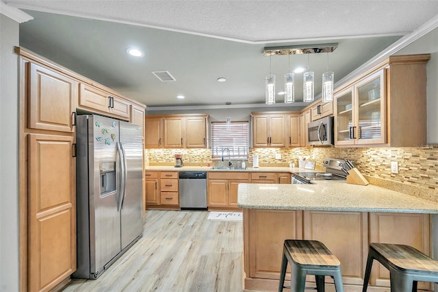 kitchen with a kitchen bar, appliances with stainless steel finishes, sink, pendant lighting, and kitchen peninsula