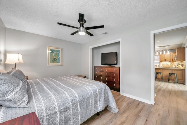 bedroom with a textured ceiling, ceiling fan, and light hardwood / wood-style floors