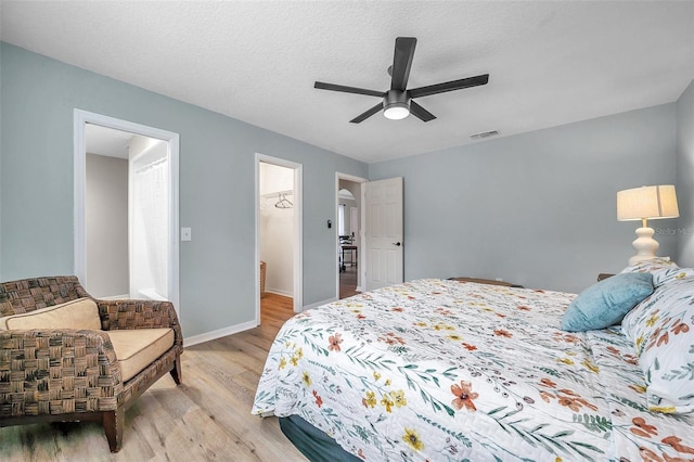 bedroom featuring light wood-type flooring, ceiling fan, a spacious closet, and a textured ceiling