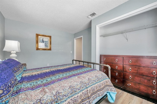 bedroom with light hardwood / wood-style floors, a textured ceiling, and a closet