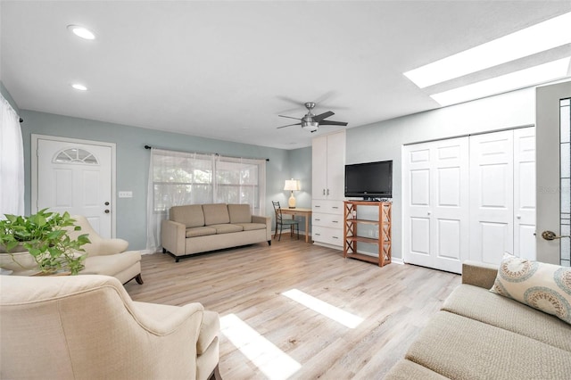 living room featuring ceiling fan, a skylight, and light hardwood / wood-style floors